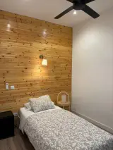 Cama individual bajo un ventilador de techo negro frente a una pared de madera